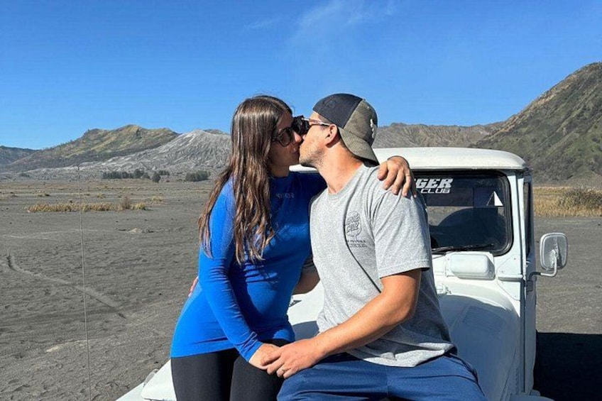A couple kissing in front of a white vehicle with 'RANGER CLUB' written on it, set against a backdrop of a barren landscape with mountains. 3