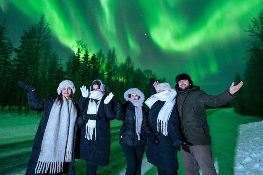 A group of people standing outdoors with a forest in the background and the aurora borealis above. 1