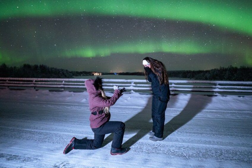 Two people on a snowy surface with a green aurora in the background. 2