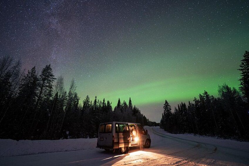 A van driving on a snowy road at night with the aurora borealis in the background. 3