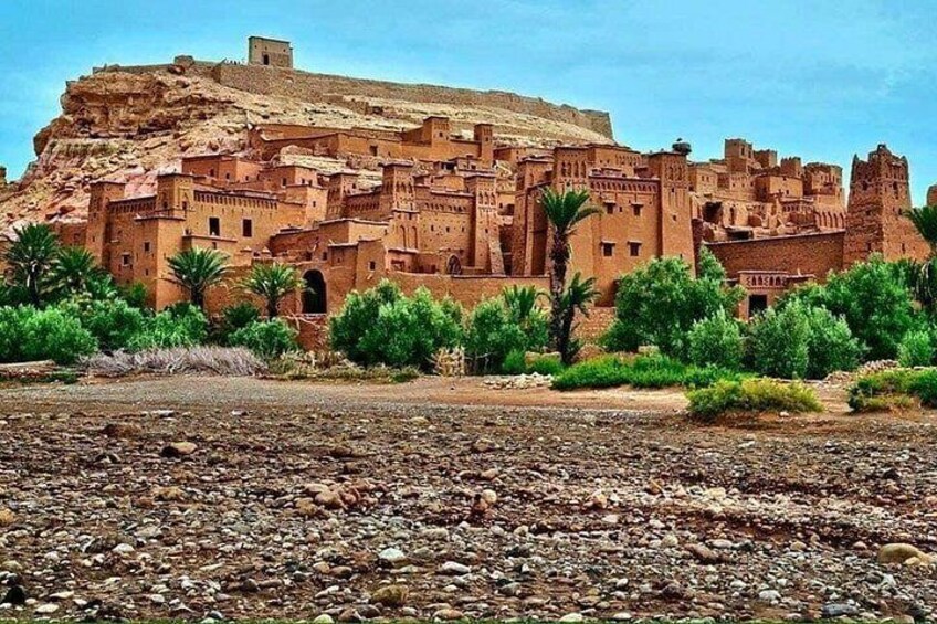A historic adobe village with terraced structures, palm trees, and a rocky foreground. 2
