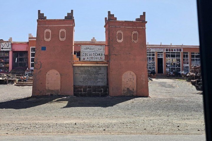 A large, rusted metal gate with two towers, a sign in a foreign language, and a building with large windows in the background. 5