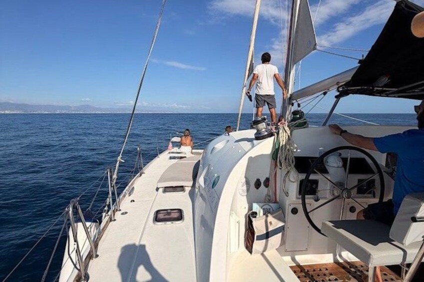 A sailboat on the water with a person standing at the stern and another person on the deck. 5