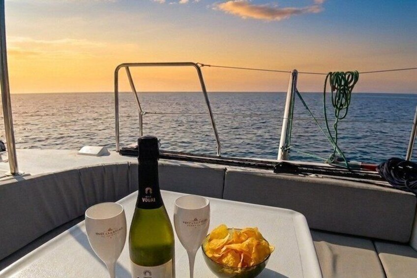A boat with a bottle of wine, two glasses, and a bowl of snacks on a table. 3