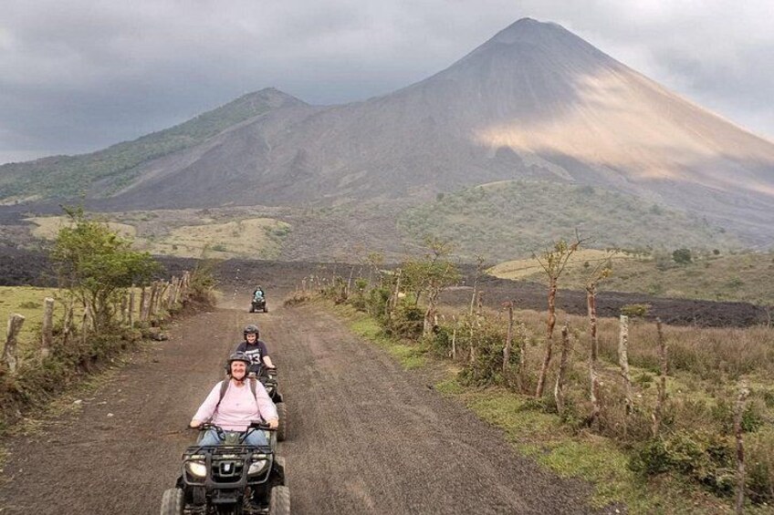 A dirt road with a person on a quad bike, a mountain in the background, and a fence on the side. 3