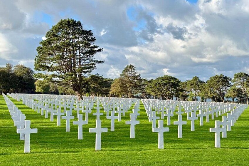 A cemetery with rows of white crosses on green grass under a cloudy sky. 3