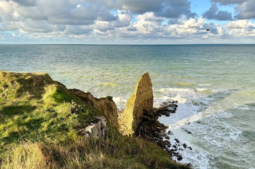 A coastal landscape with a prominent rock formation, grassy cliffs, and the ocean. 1