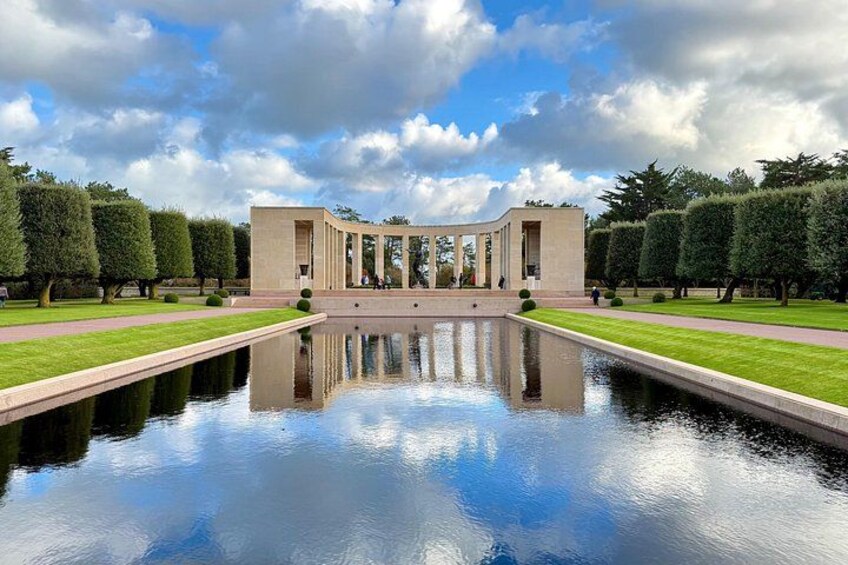 A symmetrical building with a reflective pool in front, surrounded by trimmed hedges and a clear sky. 2