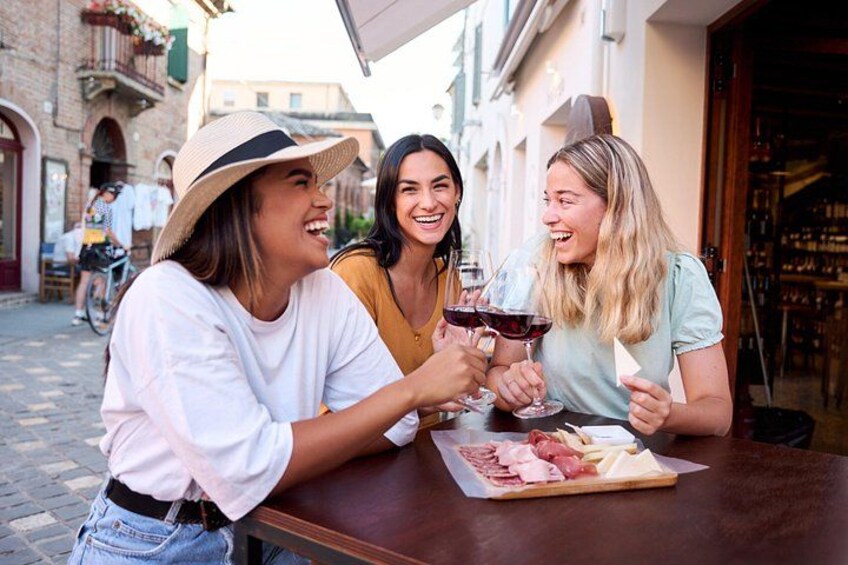 Three people toasting with wine glasses at an outdoor table with a plate of food. 1