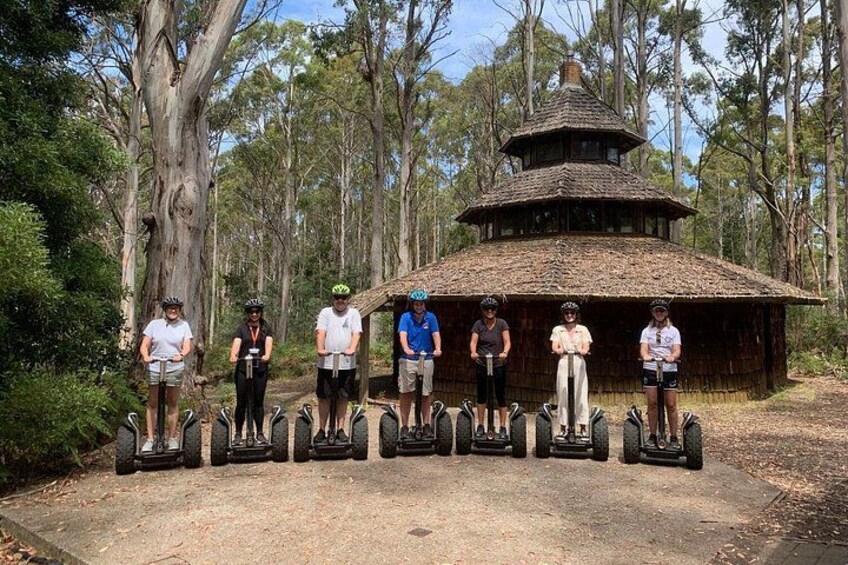 Un grupo de personas en segways en un área boscosa con una estructura de madera al fondo. 4