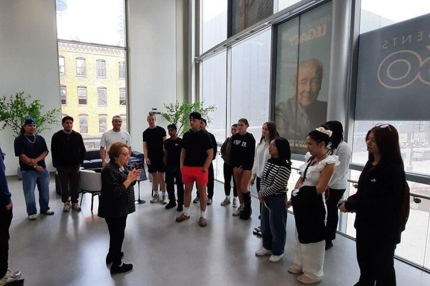 A group of people standing in a room with large windows, some facing a projection screen. 4