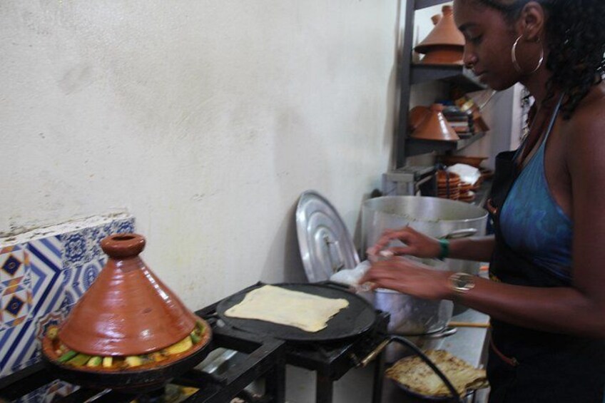 A person cooking with a tagine on a stove, a cloth on a plate, and kitchen utensils. 4