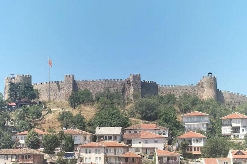 A historic stone fortress with a flag, surrounded by residential buildings on a hillside. 2