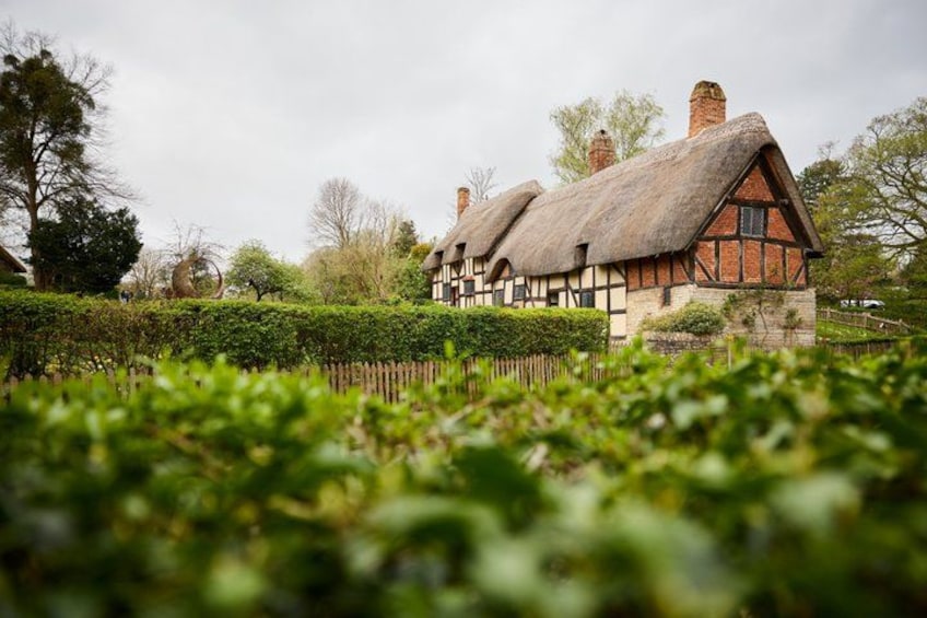 A traditional thatched-roof house with a wooden frame, surrounded by a well-maintained hedge and trees. 3