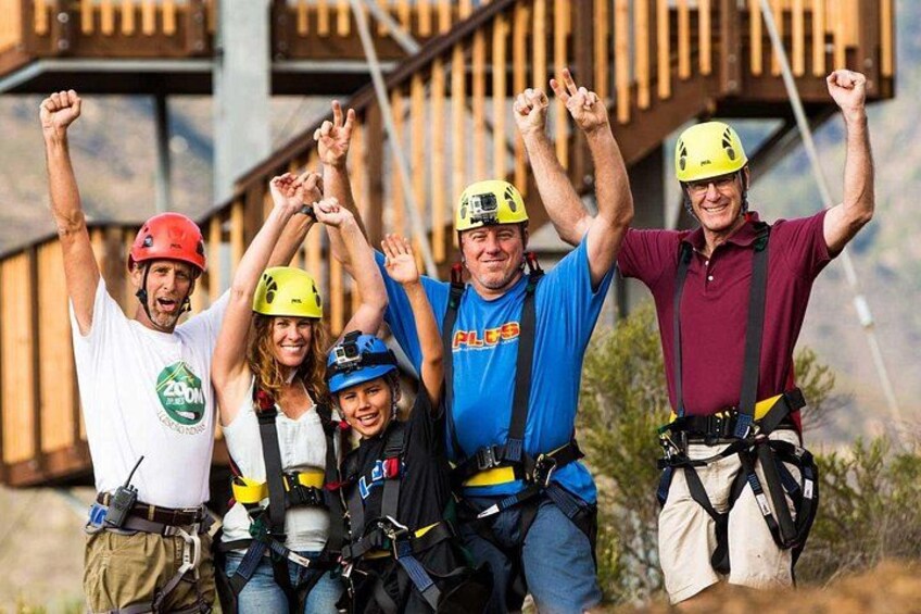 A group of people with helmets and harnesses, standing outdoors with a wooden structure in the background. 2