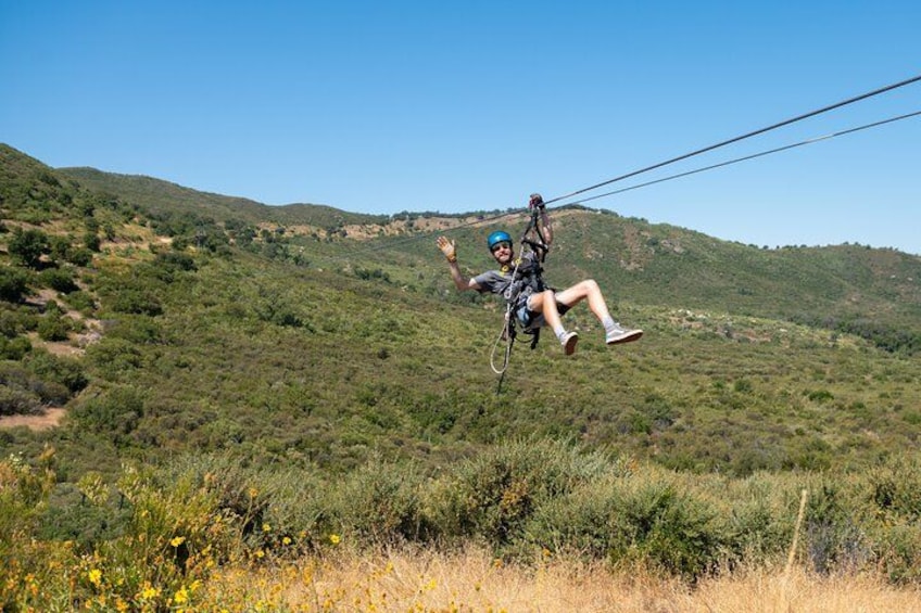 A person ziplining over a hilly landscape with sparse vegetation. 4