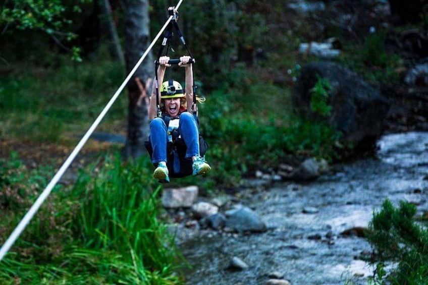 A person zip-lining over a river with greenery and rocks in the background. 3