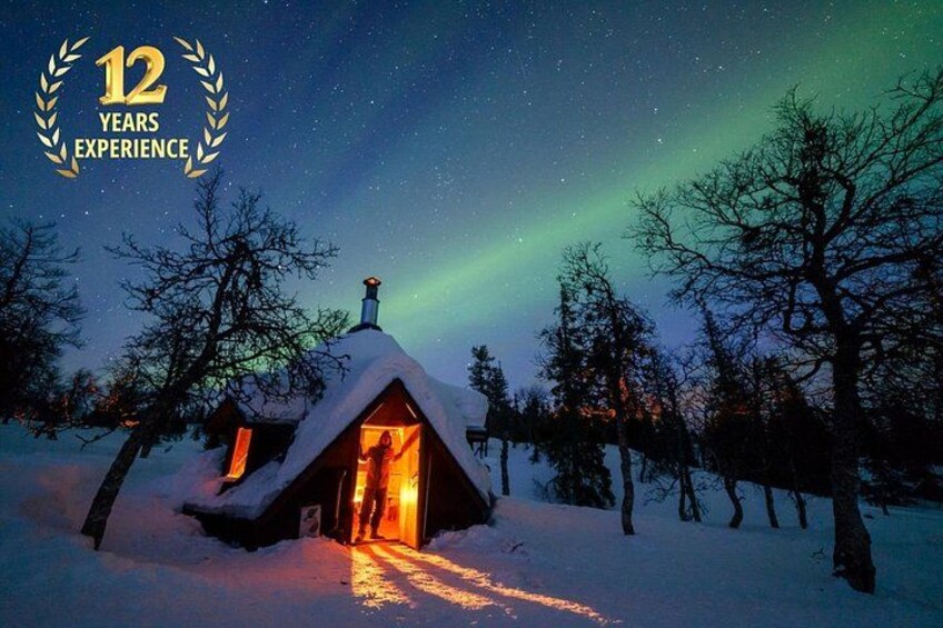 A snow-covered cabin with a lit interior, surrounded by trees and a starry night sky. 1