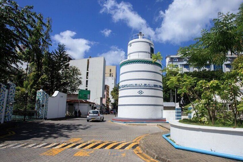 A modern building with a cylindrical tower, surrounded by trees and a paved area with yellow markings. 1