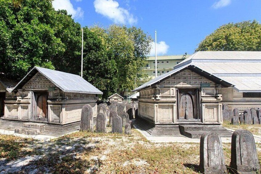 A cemetery with stone headstones and small wooden structures, likely tombs or memorials, under a clear sky. 3