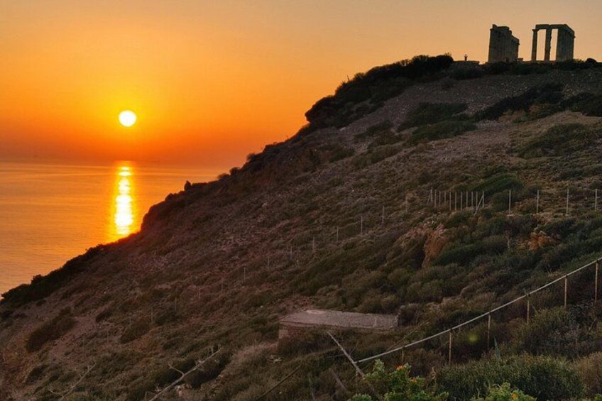 A sunset over a coastal landscape with a hill, a pathway, and ancient ruins. 4