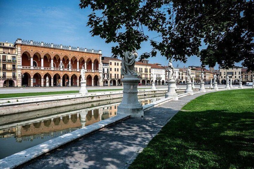 A historic building with arched windows, a reflective waterway, and statues lining the path. 5