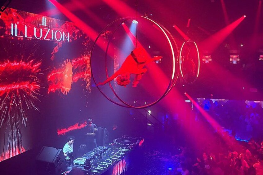 A stage with a DJ, illuminated by red and blue lights, and a large circular structure. 5
