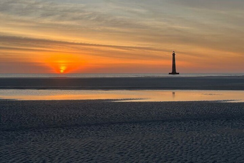 A lighthouse at sunset on a beach with calm waters reflecting the sky. 3