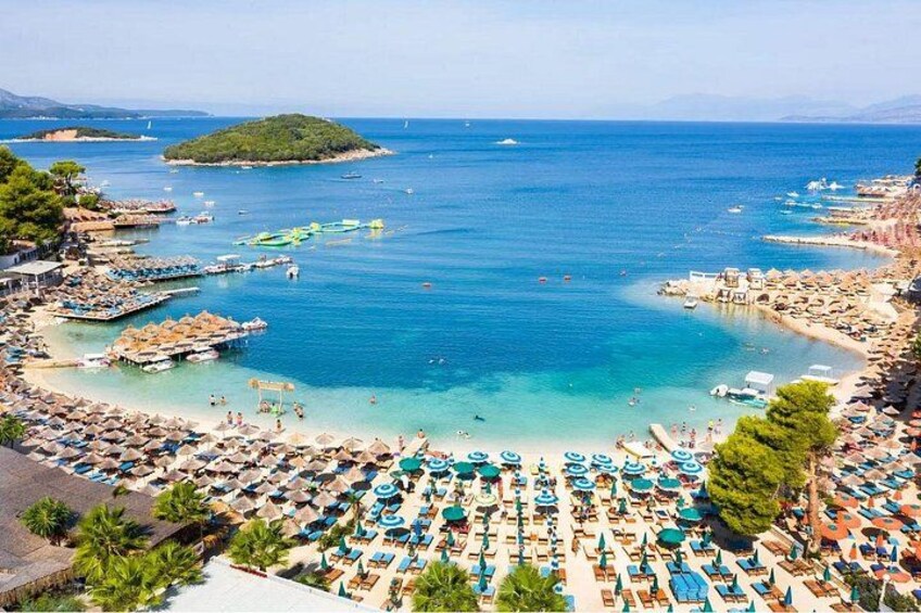 Una playa costera con numerosos sombrillas y tumbonas, barcos y un mar azul cristalino. 1