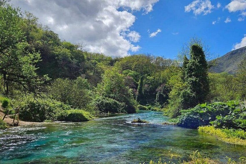Une rivière qui traverse une vallée boisée, avec des eaux claires, et qui est bordée d’une végétation luxuriante et de collines. 2