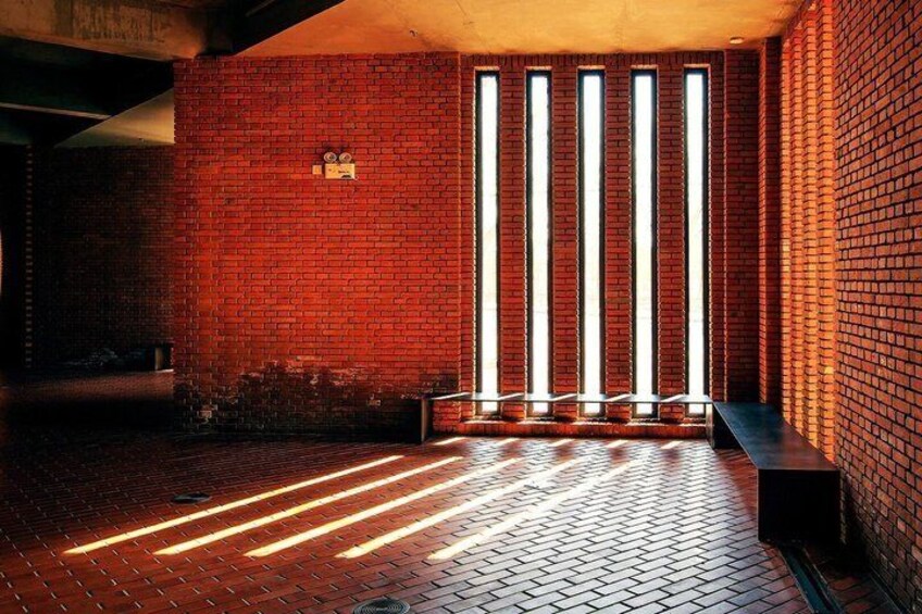 A brick-walled room with a bench and a window with vertical blinds. 2