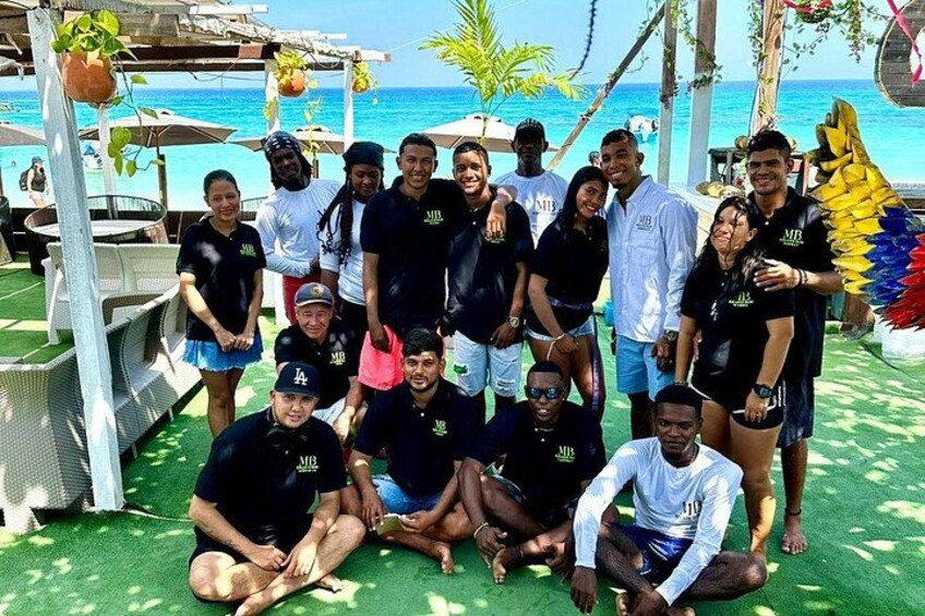 A group of people posing outdoors with a beach and ocean in the background. 2