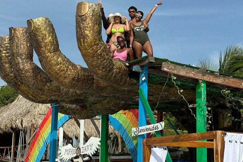 A large golden sculpture of a fish, a thatched-roof hut, and a rainbow-colored flag. 1