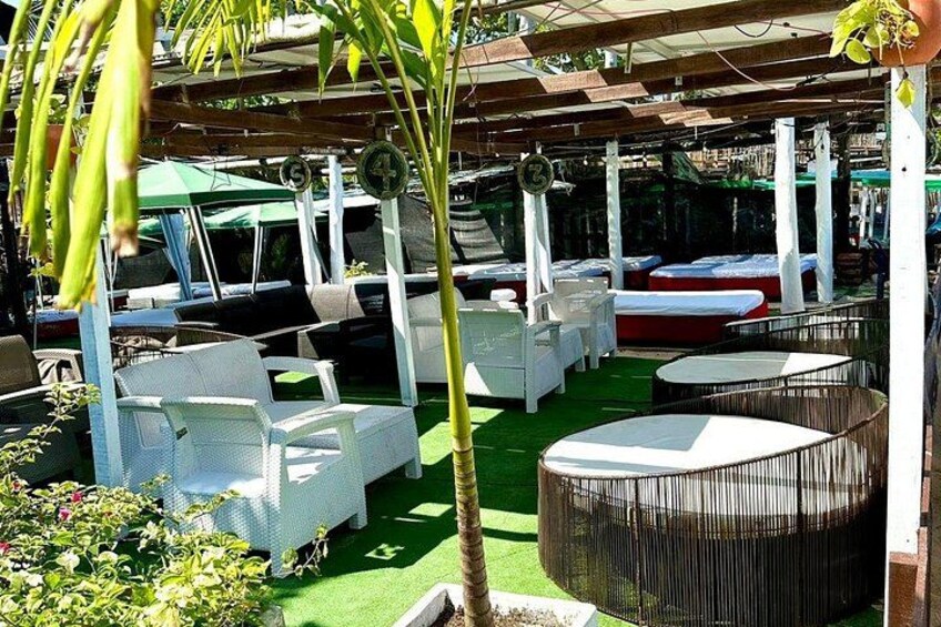 An outdoor seating area with white chairs and tables, surrounded by greenery and a palm tree. 5