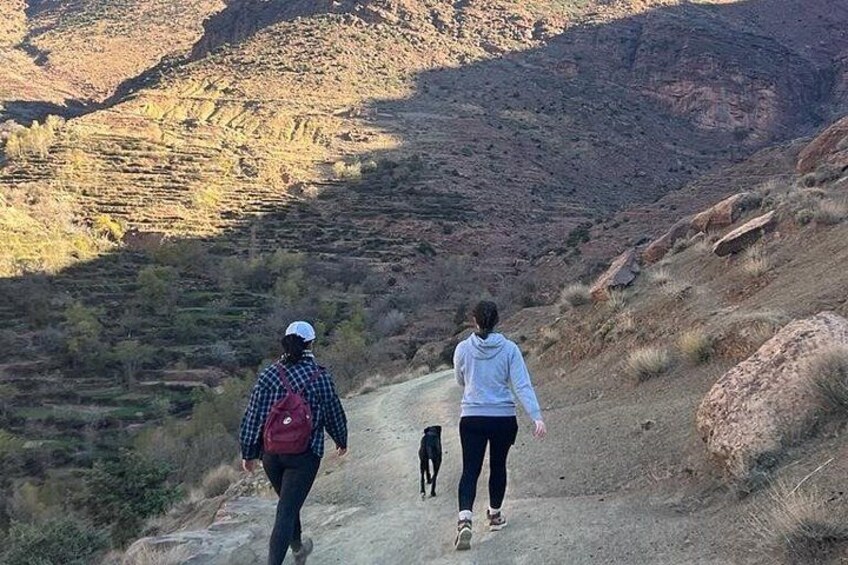 Two people walking a dog on a dirt path with a mountainous landscape in the background. 4
