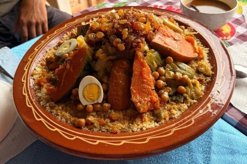 A large, ornate clay plate filled with a variety of foods including vegetables, chickpeas, and a boiled egg, suggesting a traditional meal setting. 2