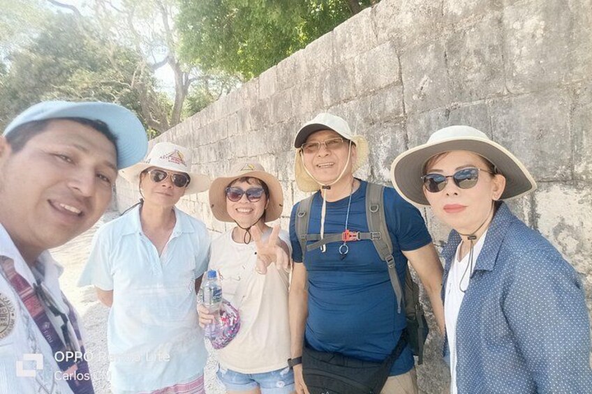 A group of people standing in front of a stone wall, some wearing hats and sunglasses. 3