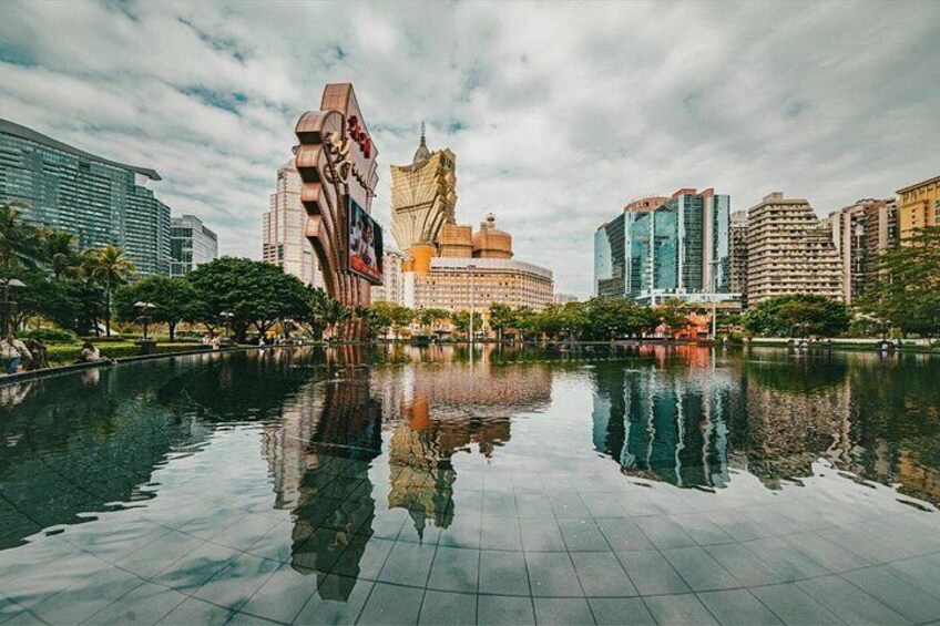 A cityscape with a large reflective water body, modern buildings, and a distinctive architectural structure. 2