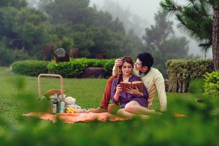 A couple sitting on a blanket in a park with a picnic basket and snacks. 1