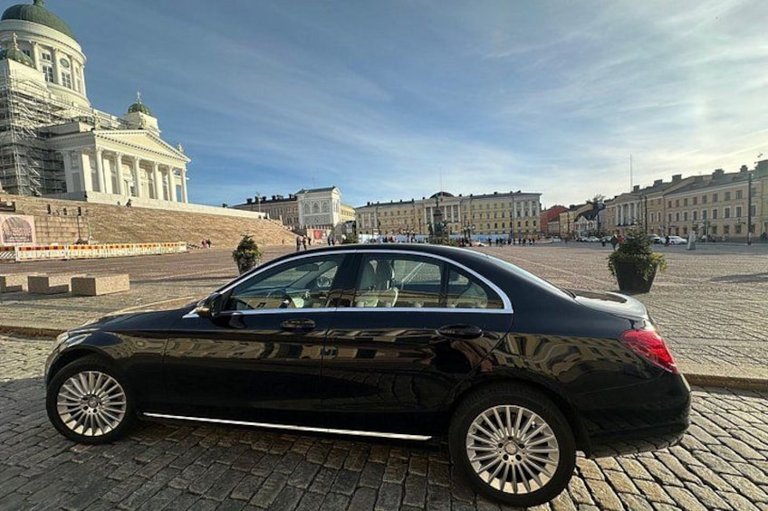 A black car parked on a cobblestone street with a large building in the background. 3
