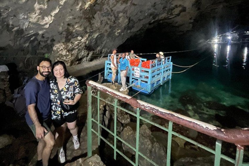 A cave entrance with a boat docked on the water, people standing on the dock, and a railing in the foreground. 2