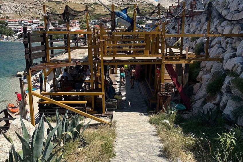 A wooden pier with a staircase leading to a platform, surrounded by rocks and plants. 3