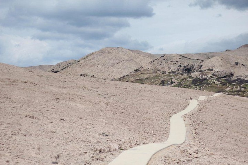 A winding dirt path through a barren landscape with hills in the background. 1