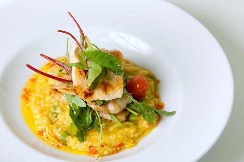 A white plate with a dish of yellow risotto, topped with greens, a cherry tomato, and a piece of fish. 2