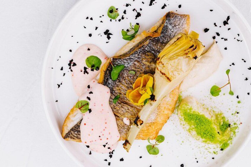 A white plate with a grilled fish, green leaves, and a pink sauce. 3