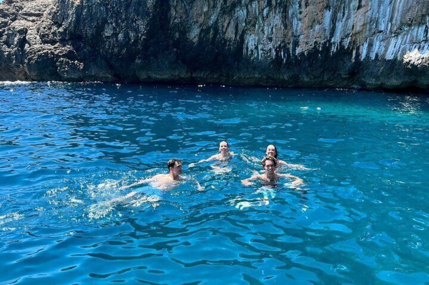 Tre personer som simmar i en klarblå pool med branta klippor i bakgrunden. 1