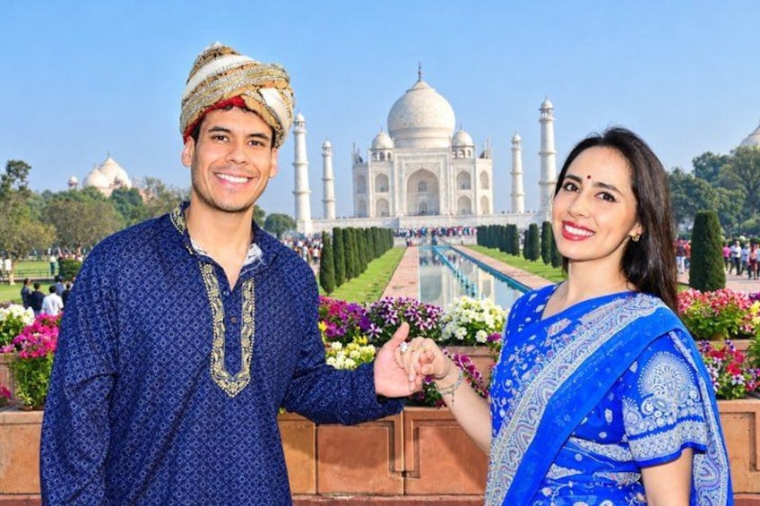 Ett par i traditionella kläder som håller varandra i handen framför Taj Mahal. 5