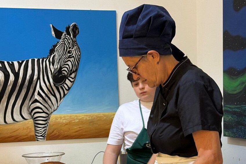 A person wearing a hat and apron, standing next to a painting of a zebra. 3