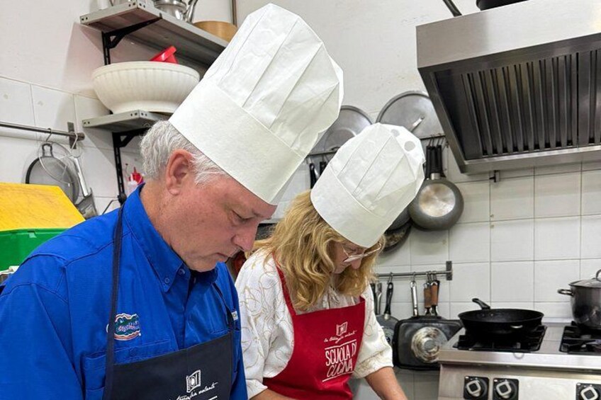 Two people in a kitchen, one wearing a chef's hat and apron, and the other in a blue uniform. 2