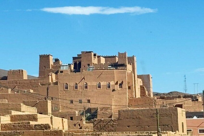 A large, multi-story building with a fortress-like appearance, situated on a hill with a clear blue sky above. 3